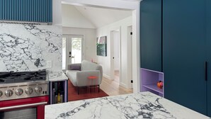 Una cocina moderna con encimera de mármol, estufa roja y comedor con sofá gris y detalles en rojo.