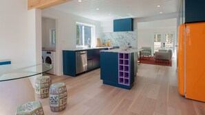 Una cocina moderna con una isla central, un comedor con mesa de vidrio y una sala de estar con sofá y sillones.