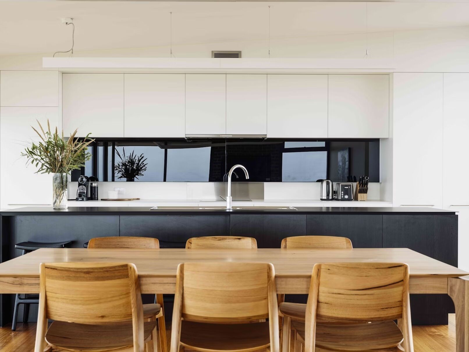 A modern kitchen with white cabinets, a black backsplash, and a central island with a sink.