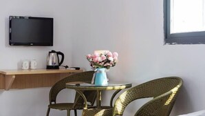 A room with a round table, wicker chairs, a wall-mounted TV, a shelf with a kettle and mugs, and a vase with flowers. - Yijia Apartment (Xiamen Airport) (Xiamen)