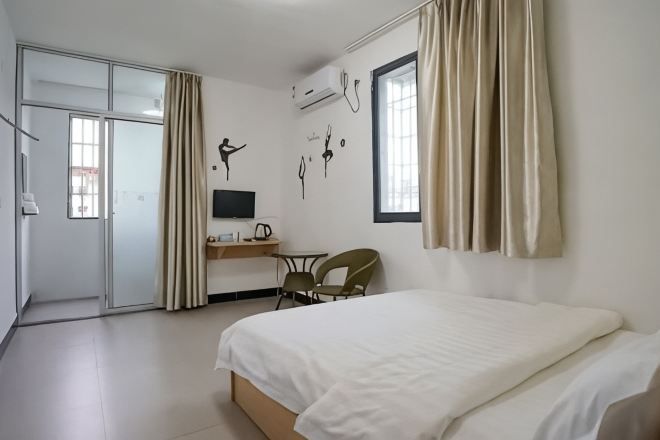 Habitación de hotel con cama, escritorio, silla, televisor y cortinas.