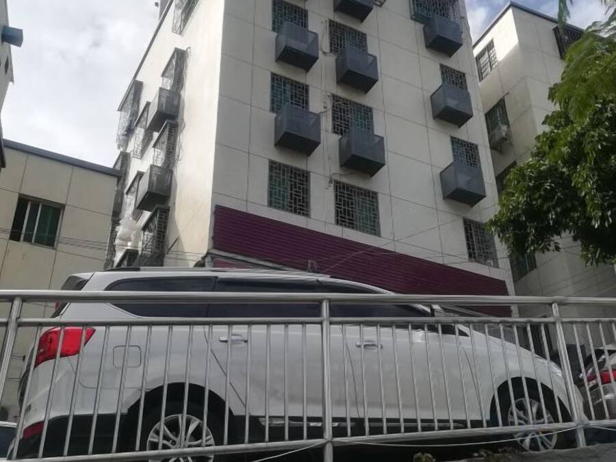 Edifício residencial de vários andares com varandas, portão fechado e um carro estacionado.