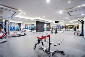 A modern gym with various exercise equipment, a large mirror, and a wall with a sports-themed mural. - Bloomfields Cozy Studio In Hera Tower (Dubai)
