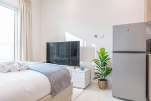 A hotel room with a bed, a television, a refrigerator, and a potted plant. - Bloomfields Cozy Studio In Hera Tower (Dubai)