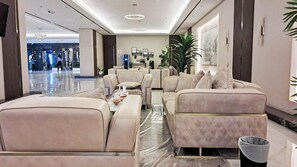 A spacious lobby with a reception desk, seating area with sofas and armchairs, and a large potted plant. - Bloomfields Cozy Studio In Hera Tower (Dubai)