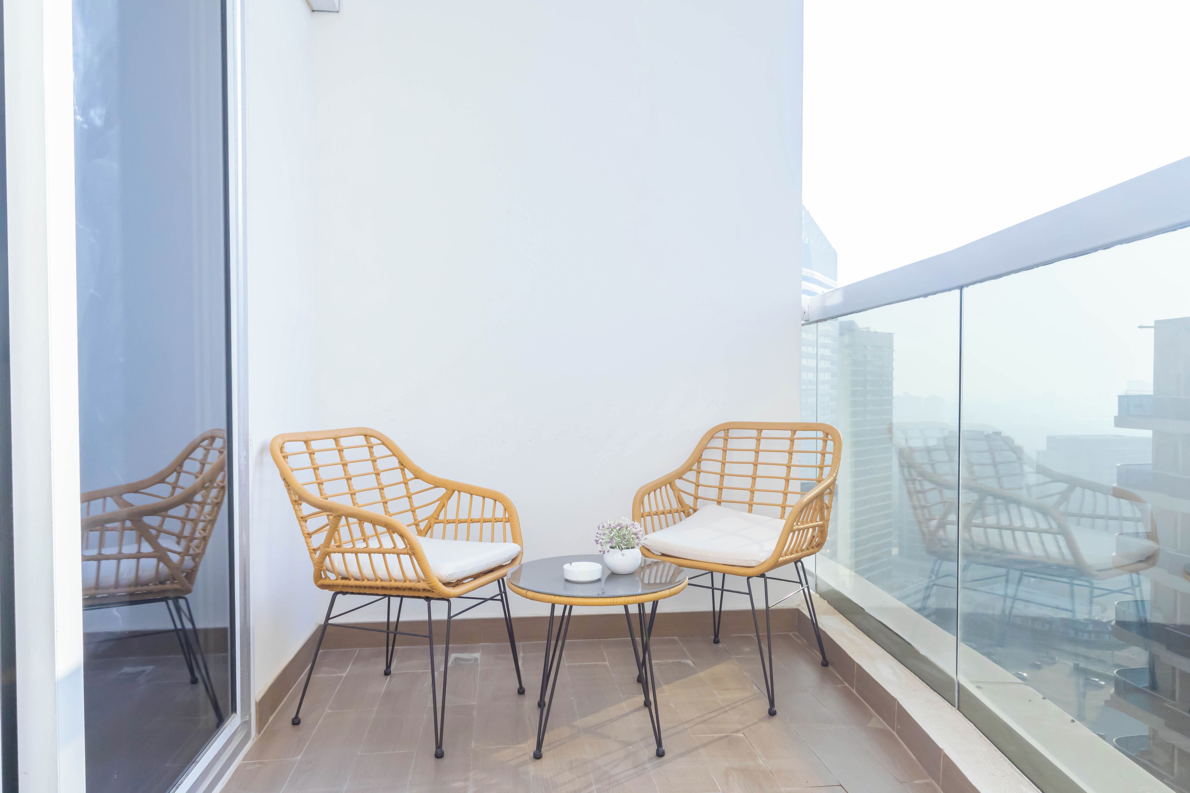 A balcony with two wicker chairs, a small table, and a potted plant.