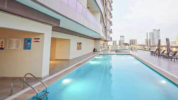 Une piscine intérieure avec vue sur les gratte-ciel de la ville, un espace de détente au bord de la piscine et un panneau de sécurité sur le mur.