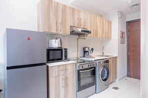 A compact kitchen with a refrigerator, microwave, stove, oven, and washing machine. - Bloomfields Cozy Studio In Hera Tower (Dubai)