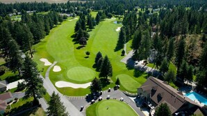 Ein Golfplatz mit Clubhaus, umgeben von dichtem Wald und Bergen im Hintergrund.