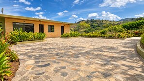 Un edificio moderno con un patio empedrado, rodeado de exuberante vegetación y un paisaje montañoso.