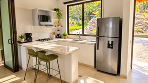 Una cocina moderna con una isla central, taburetes de bar, un refrigerador de acero inoxidable y una ventana con vistas a zonas verdes.