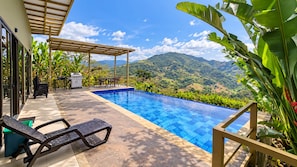 Una piscina con vistas a las montañas, un porche cubierto y mobiliario de exterior.