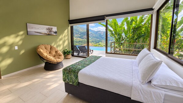 Un dormitorio con una cama grande, una silla, vistas a una piscina y montañas.