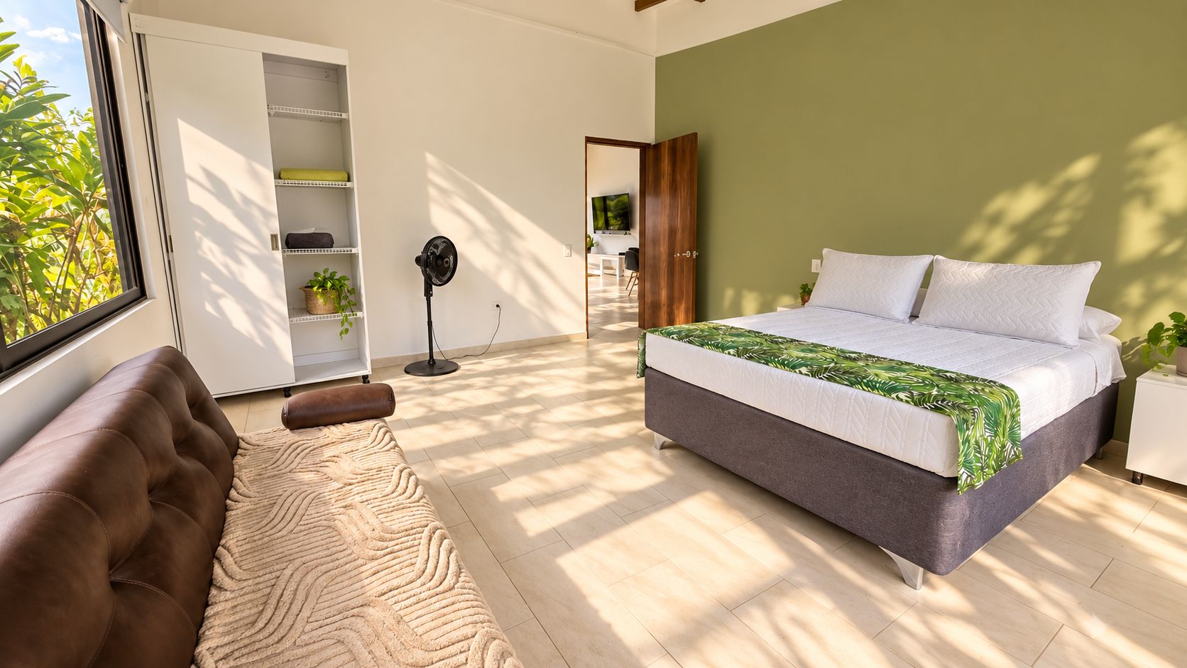 A bedroom with a bed, a sofa, a floor lamp, and a TV in the background.
