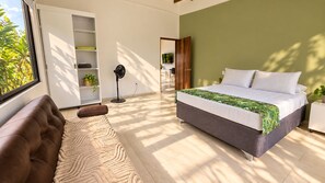 Un dormitorio con cama, sofá, lámpara de pie y televisor al fondo.