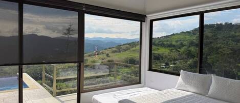 Un dormitorio con una cama grande, dos ventanas y un balcón con piscina.