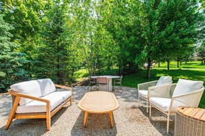 Un espace extérieur aménagé avec des meubles en osier et une table en bois, entouré d’une végétation luxuriante.