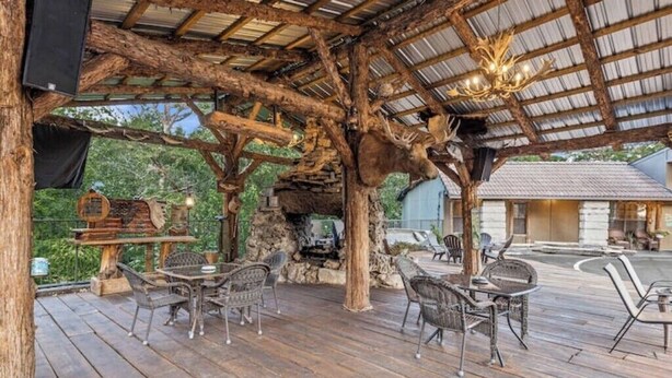 An outdoor wooden deck with rustic furniture and a stone fireplace. - 2 Queen Beds  Fast WiFi 50" TV  Salt Water Pool (Eureka Springs)