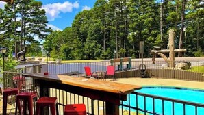 An outdoor pool area with a wooden deck, red bar stools, and a fenced play structure. - 2 Queen Beds  Fast WiFi 50" TV  Salt Water Pool (Eureka Springs)