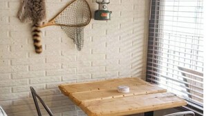 A rustic interior with a wooden table, a chair, a small stool, a cat's tail hanging from a net, and a wall-mounted heater. - 2 Queen Beds  Fast WiFi 50" TV  Salt Water Pool (Eureka Springs)