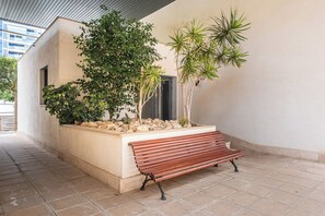 A bench in a covered outdoor area with a tiled floor, surrounded by plants and a small rock garden. - Tamarindo Apartment 6p - Playa La Cala Beach (VC)