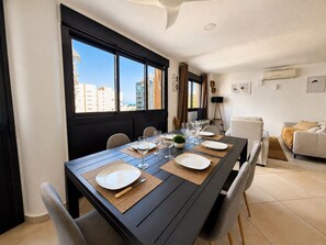 A dining area with a long table set for four, large windows with a city view, and a modern interior design.