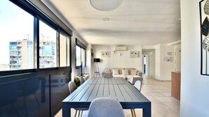 A modern living room with a large window, a dining table, and a sofa.