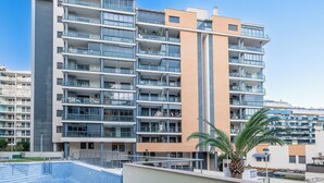 A multi-story residential building with balconies, a swimming pool, and a palm tree.