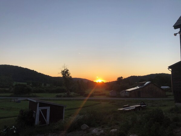 Paisaje rural al atardecer con un granero, un cobertizo pequeño y una caravana en primer plano.