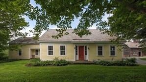 Une maison à deux étages avec une porte rouge, un porche à l’avant et une pelouse bien entretenue.