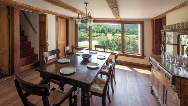 Une salle à manger avec une grande table en bois, des chaises et une vue sur un lac, visible à travers de grandes fenêtres.
