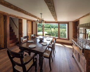 Comedor con una gran mesa de madera, sillas y vista a un lago a través de amplios ventanales.