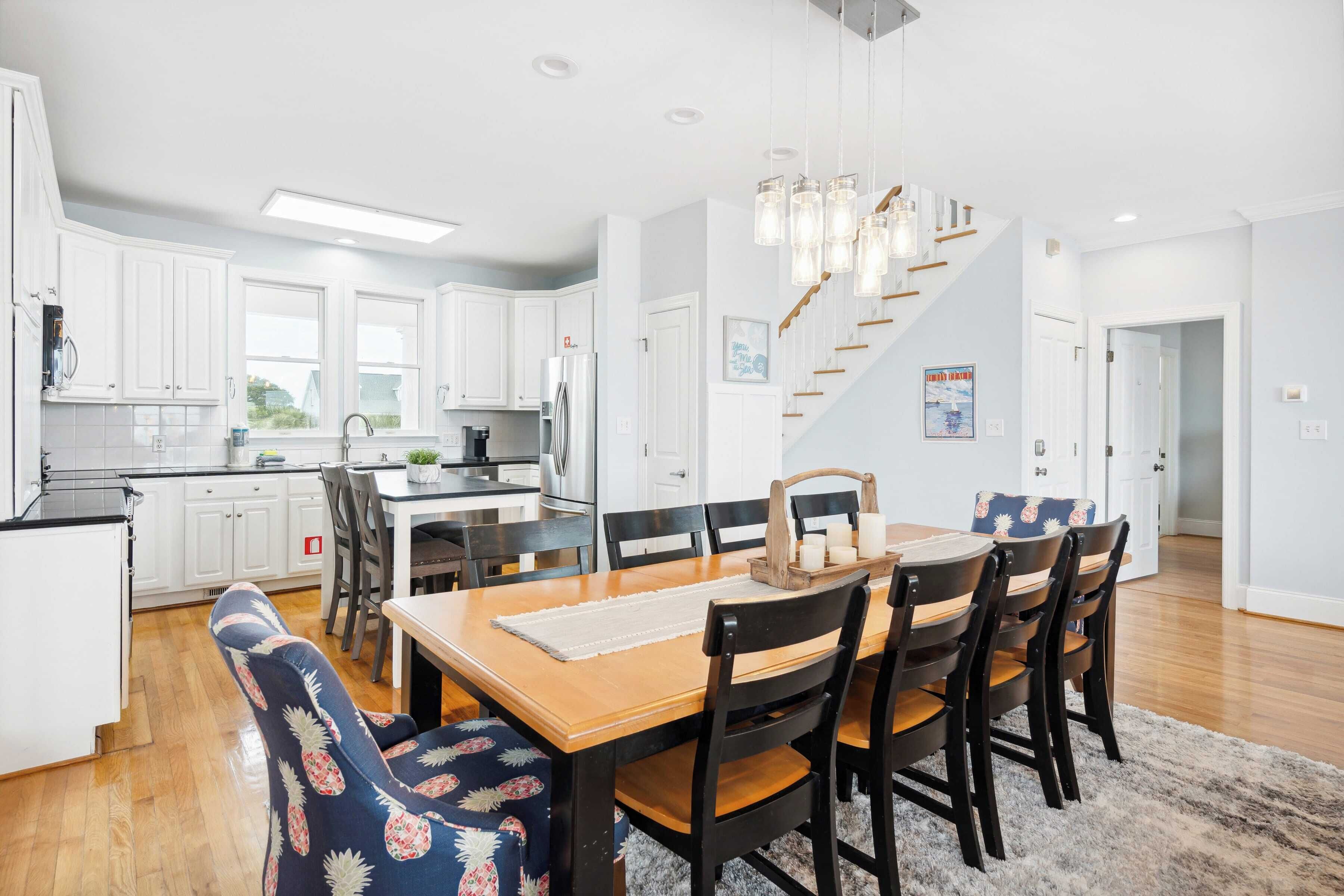 A modern kitchen with white cabinets, a wooden dining table, and a staircase leading to another level.