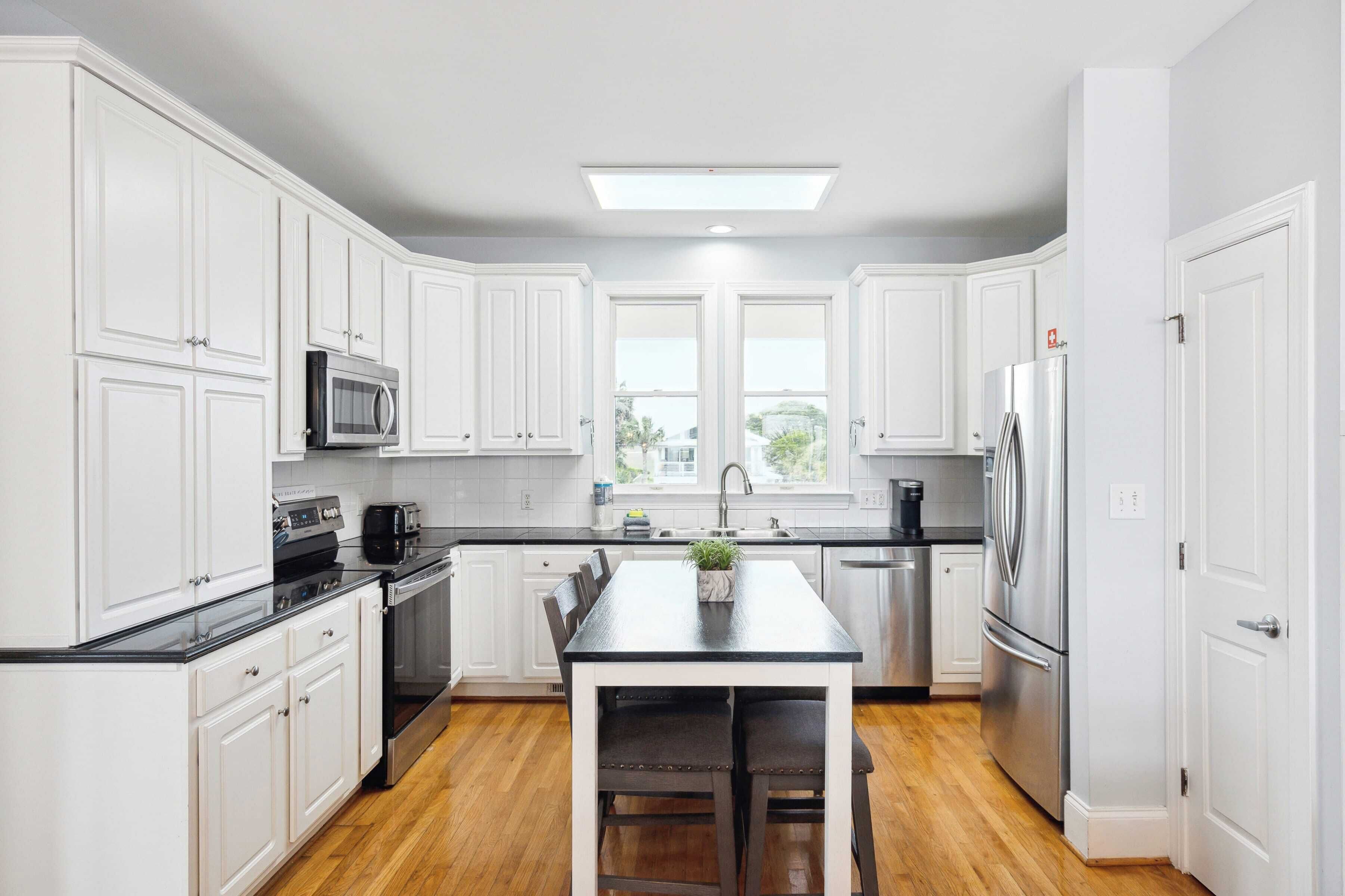 A modern kitchen with white cabinetry, a black countertop, stainless steel appliances, and a central island with seating.