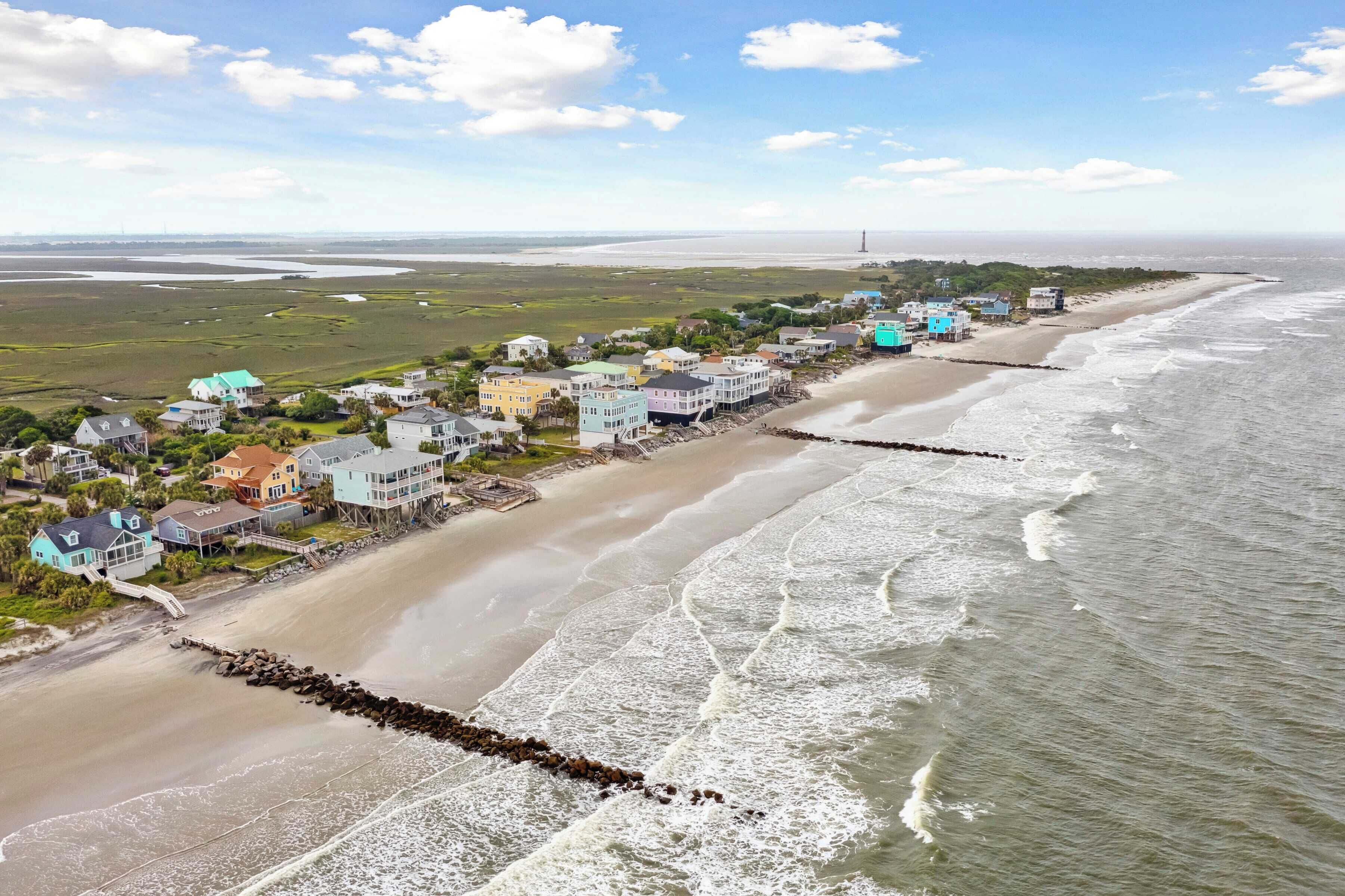 A coastal residential area with houses along the beach, a rocky breakwater, and a clear view of the ocean.