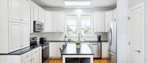 Una cocina moderna con armarios blancos, encimera negra, electrodomésticos de acero inoxidable y una ventana con vistas a zonas verdes.