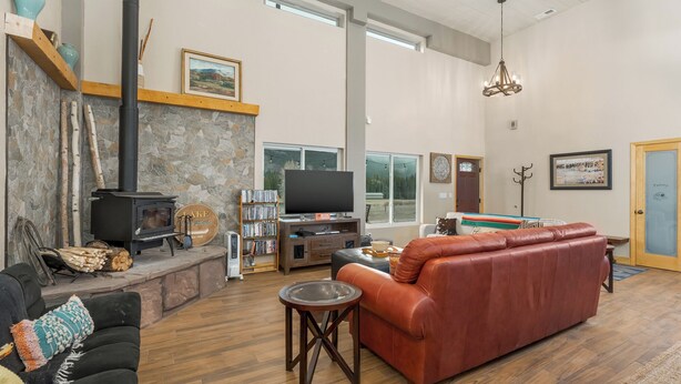 A spacious living room with a stone fireplace, a television, a leather sofa, and a bookshelf. - Pond Property with Mountain Views (Bayfield)