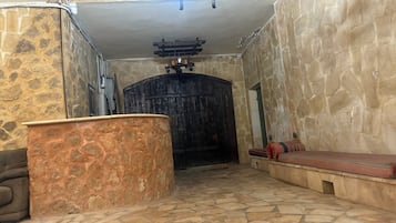 Un pasillo de paredes de piedra con una puerta de madera grande, un banco de piedra y una pequeña mesa.
