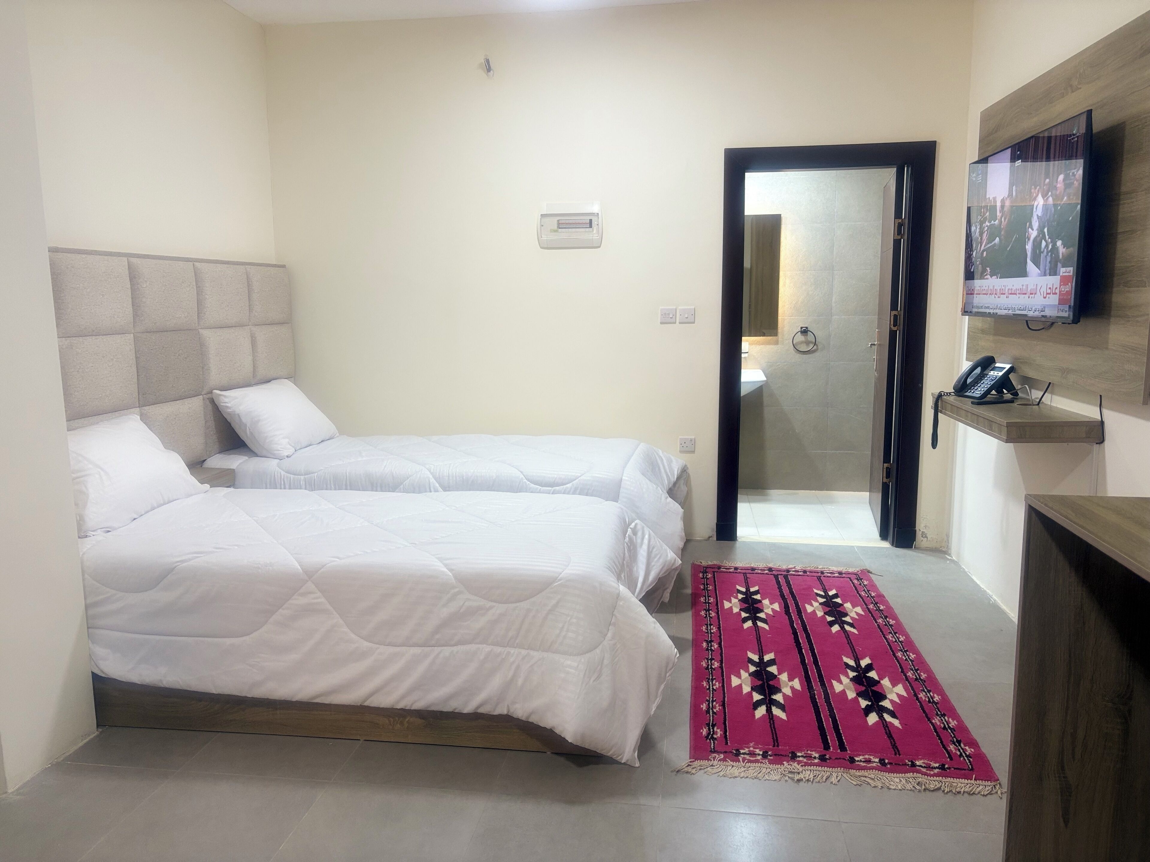 A hotel room with two beds, a TV, a phone, and a bathroom visible through an open door.