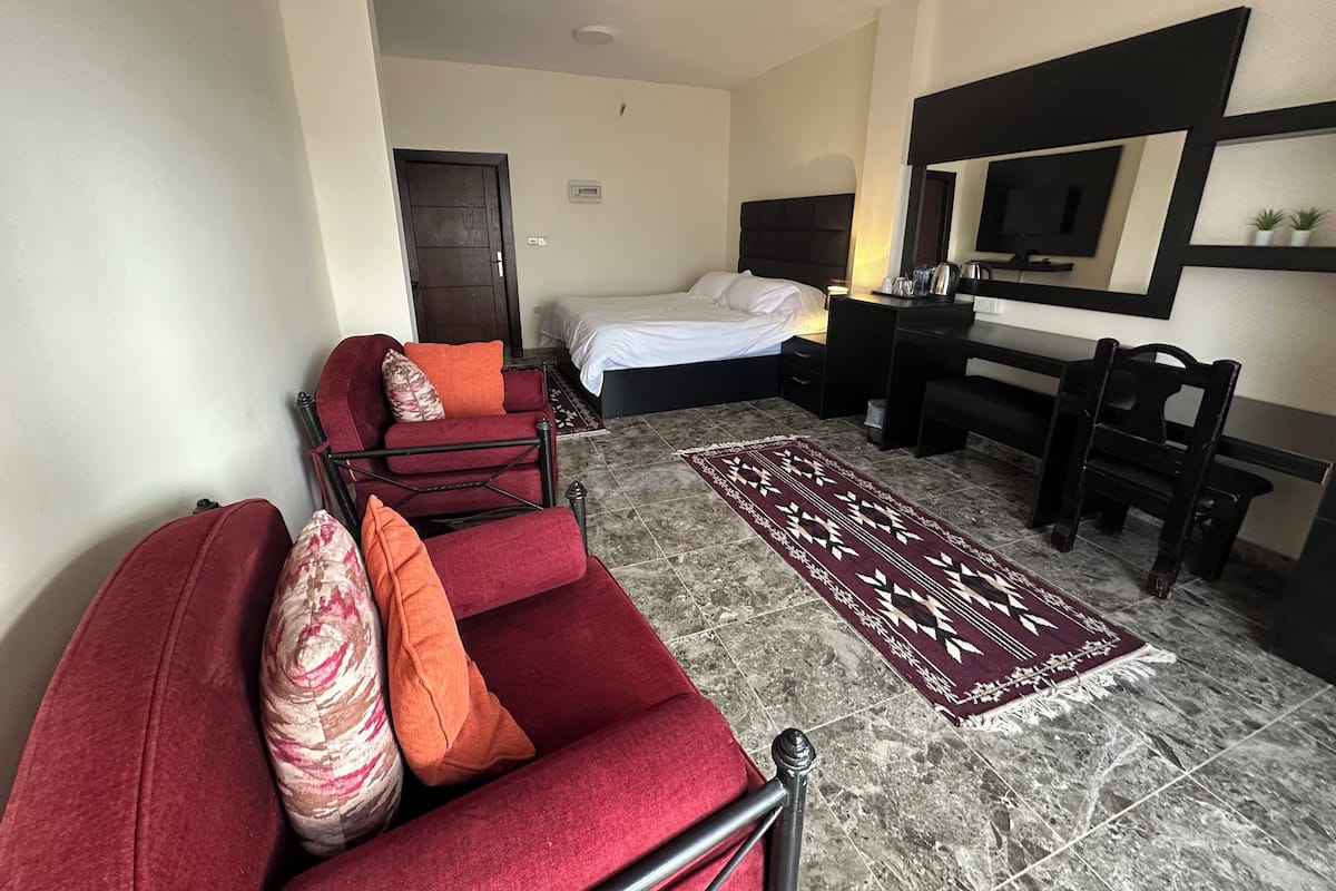A hotel room with a bed, a desk, a chair, a sofa, and a rug.
