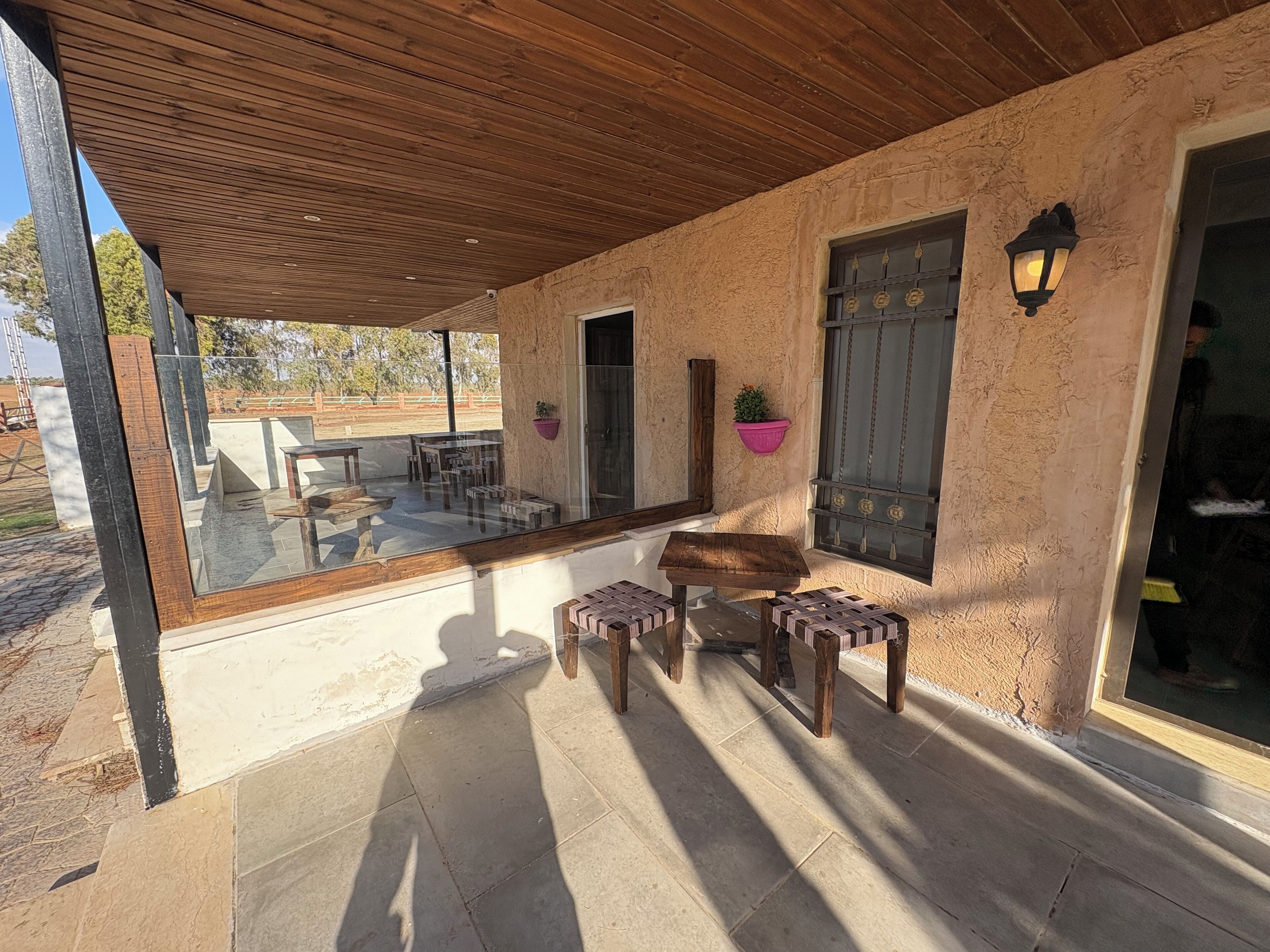 Un patio cubierto con suelo de madera, pared de vidrio y un conjunto de mesas y sillas.