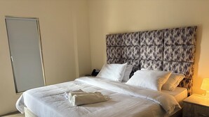 A neatly made bed with white linens and pillows, a patterned headboard, a bedside phone, and a nightstand with a lamp. - Qastal Zaman (Amman)