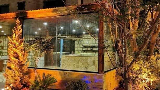 A modern building with a glass facade, surrounded by landscaped gardens and a stone-paved area. - Qastal Zaman (Amman)