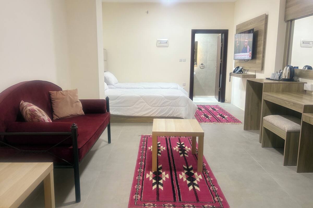 A hotel room with a bed, a red sofa, a wooden desk, and a TV.