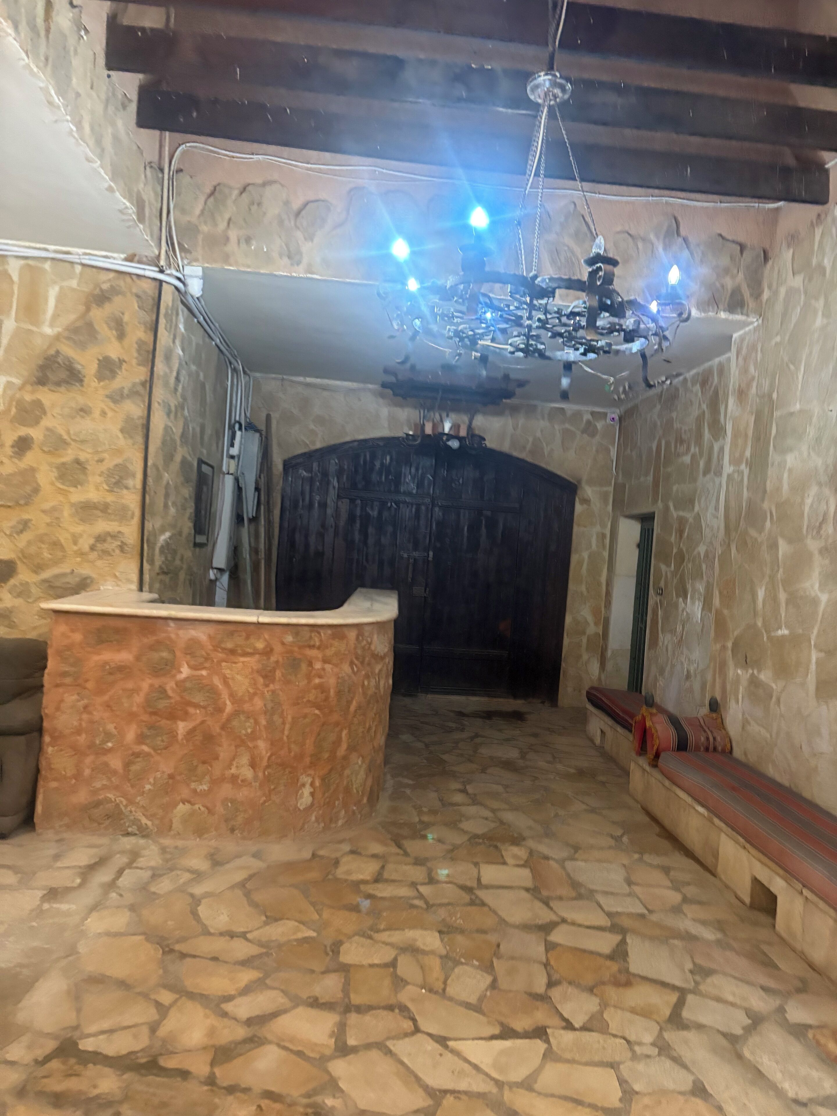 Habitación con paredes y suelo de piedra, un banco de madera, un banco de piedra y una pared de piedra con una puerta.