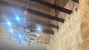 A stone-walled room with a wooden bench, a chandelier, and a large wooden door. - Qastal Zaman (Amman)