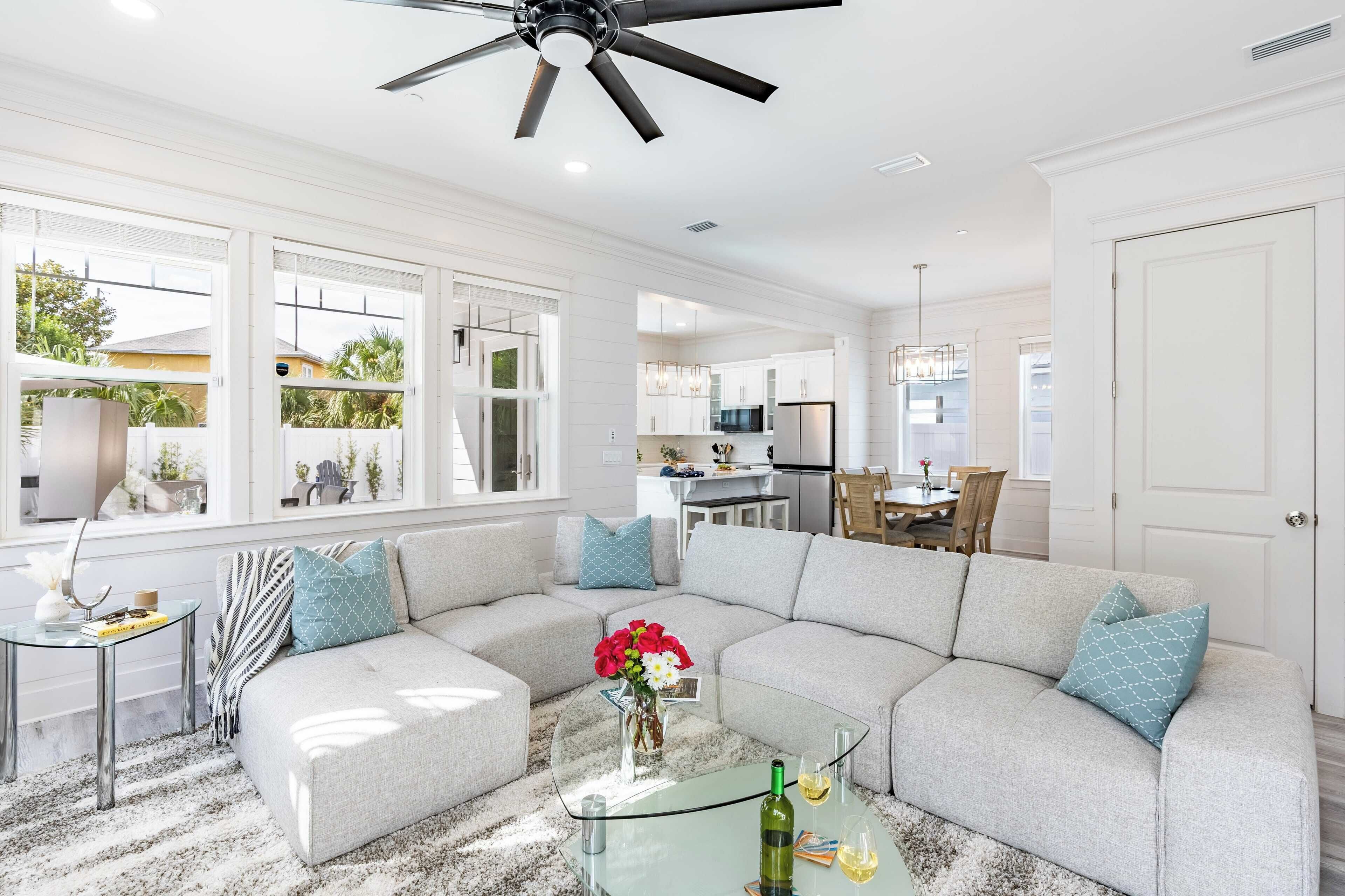 A modern living room with a sectional sofa, a glass coffee table, and a ceiling fan.