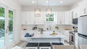 A modern kitchen with white cabinetry, a central island, pendant lights, and a view of the outdoors. - Modern 5bdr w/ Private Pool, 2 min Walk to the Beach! Montoute by Avantstay (Panama City Beach)
