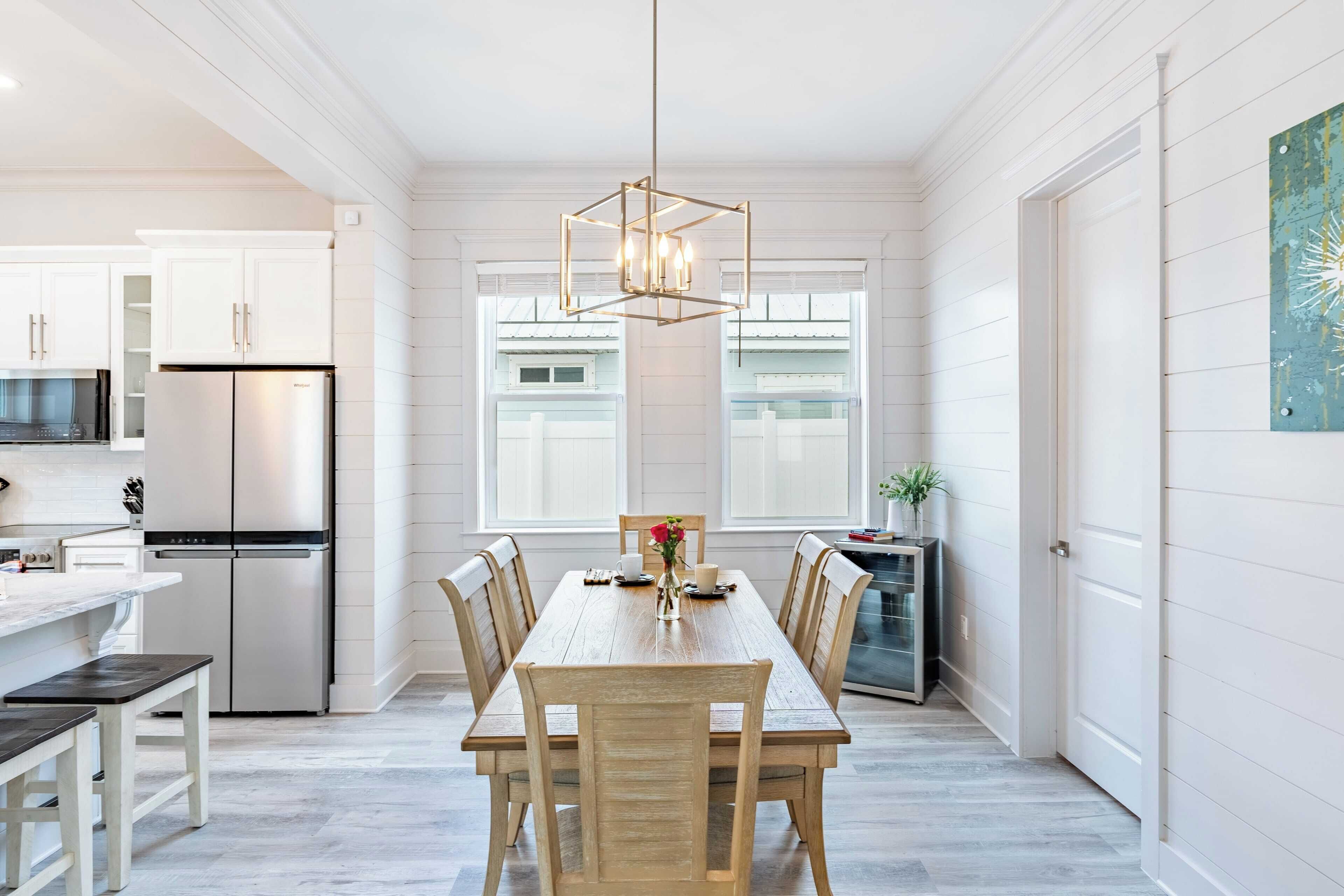 A modern kitchen with white cabinetry, a stainless steel refrigerator, and a dining area with a wooden table and chairs.