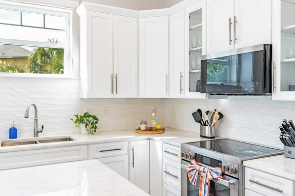 Una cocina moderna con armarios blancos, un lavamanos de acero inoxidable, un microondas y un horno.